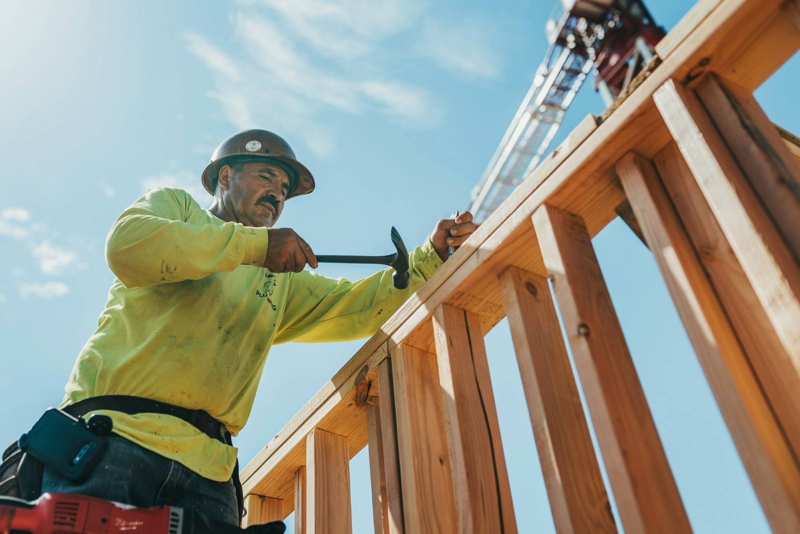 A framer working on a timber build under a blue sky