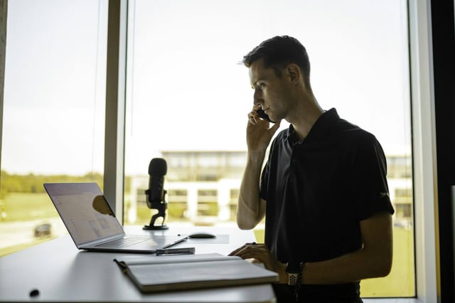 A man on the phone at a bright window desk with papers