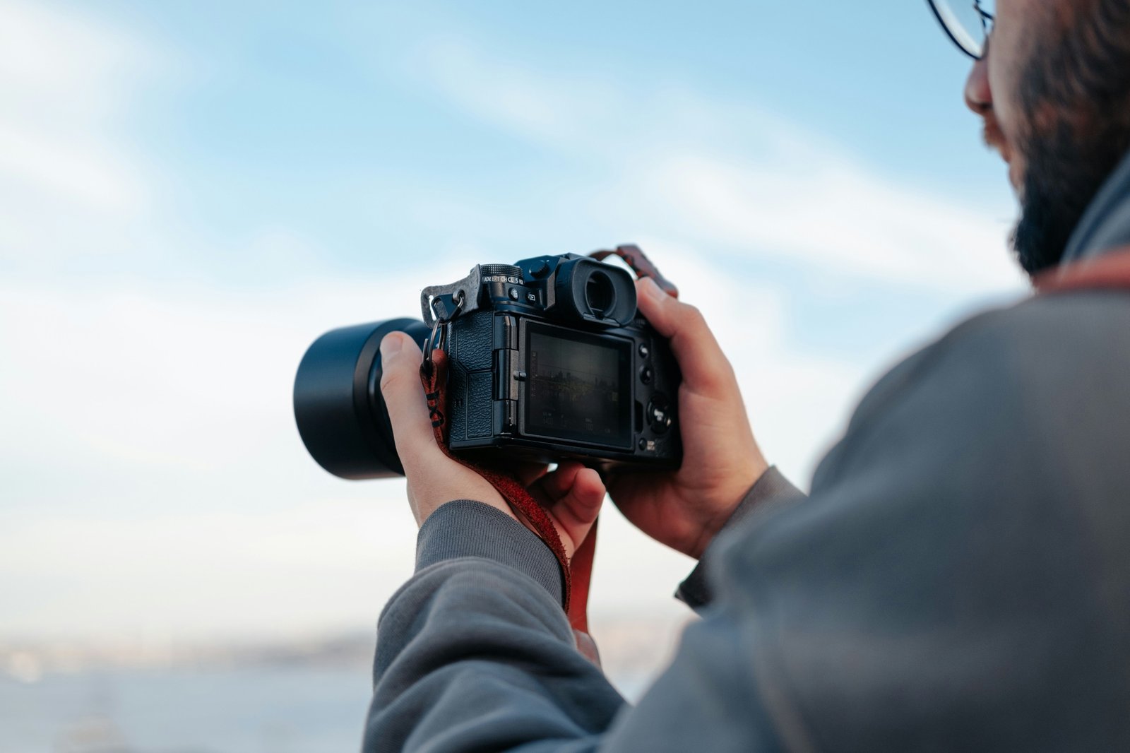 Hands holding a mirrorless camera against a bright sky