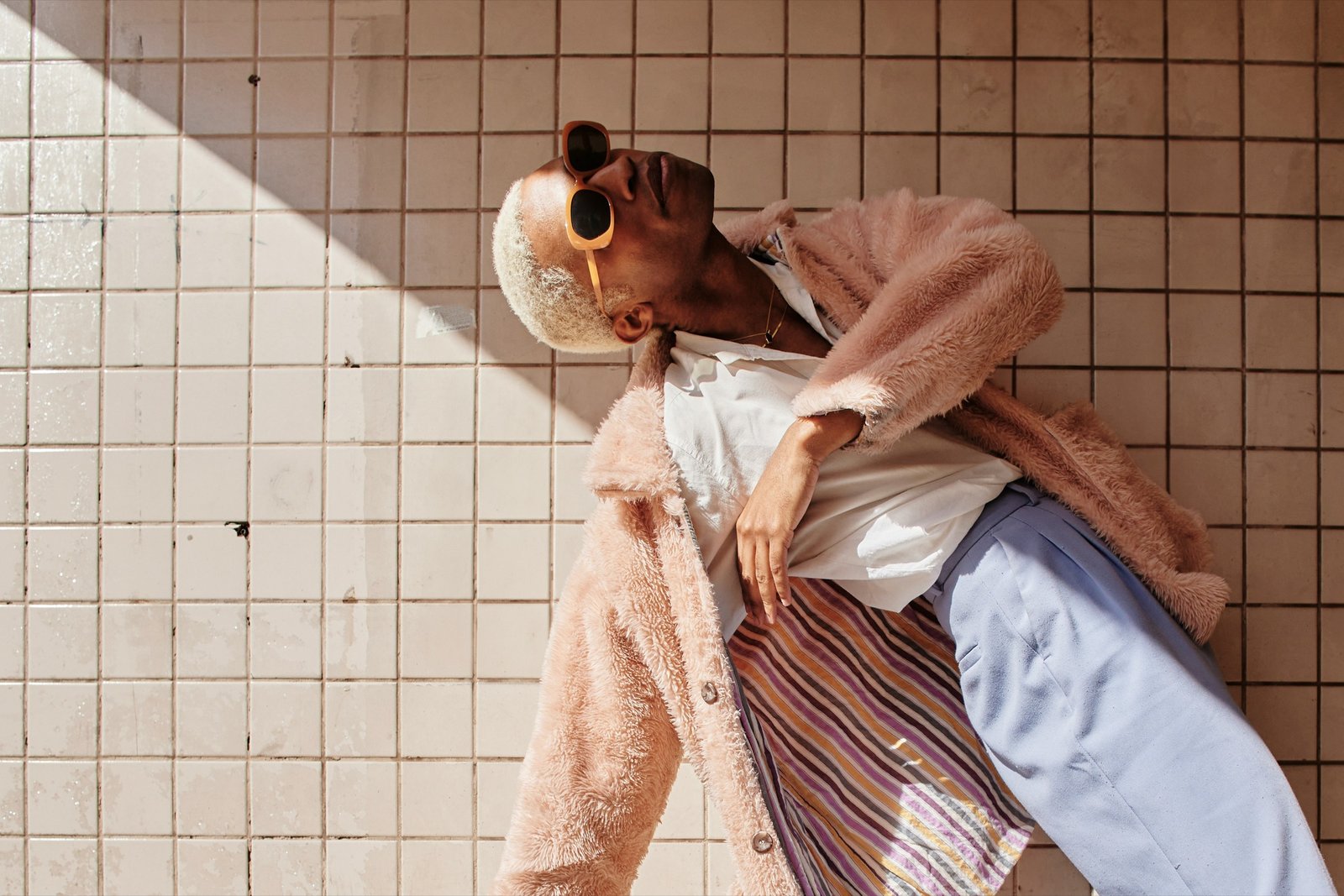 Man in a pink fur coat leaning against a tiled wall