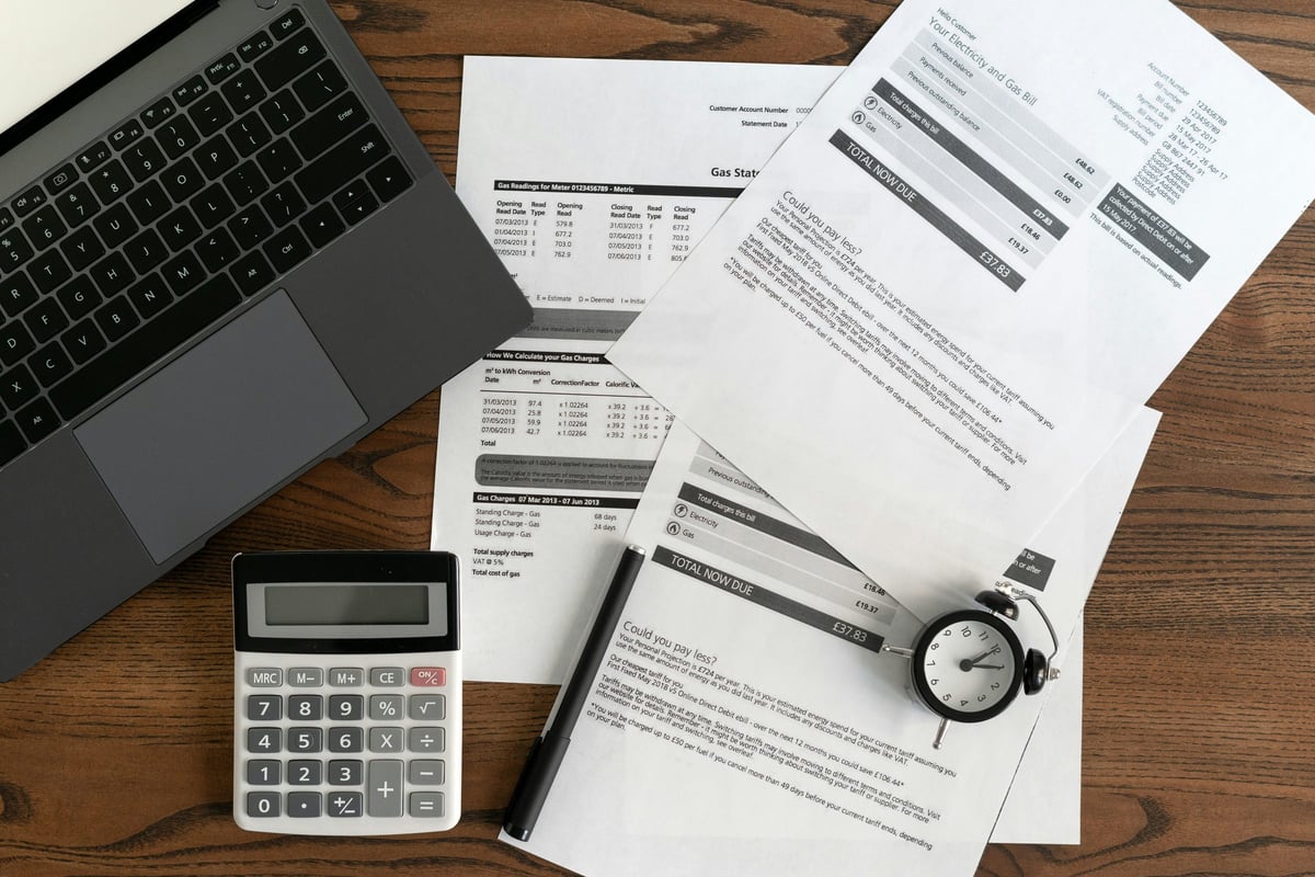 Top view of laptop computer, documents, financial bills, alarm clock, calculator and stationery on wooden table in office