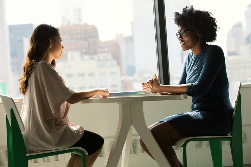 Two women talking at a table by a city window